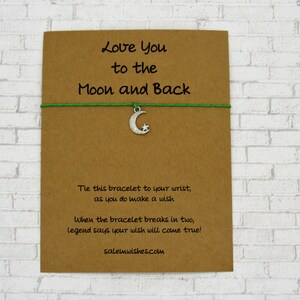 May include: A green string bracelet with a silver crescent moon charm. The card reads "Love You to the Moon and Back". Tie this bracelet to your wrist as you do make a wish. When the bracelet breaks in two, legend says your wish will come true! salemwishes.com