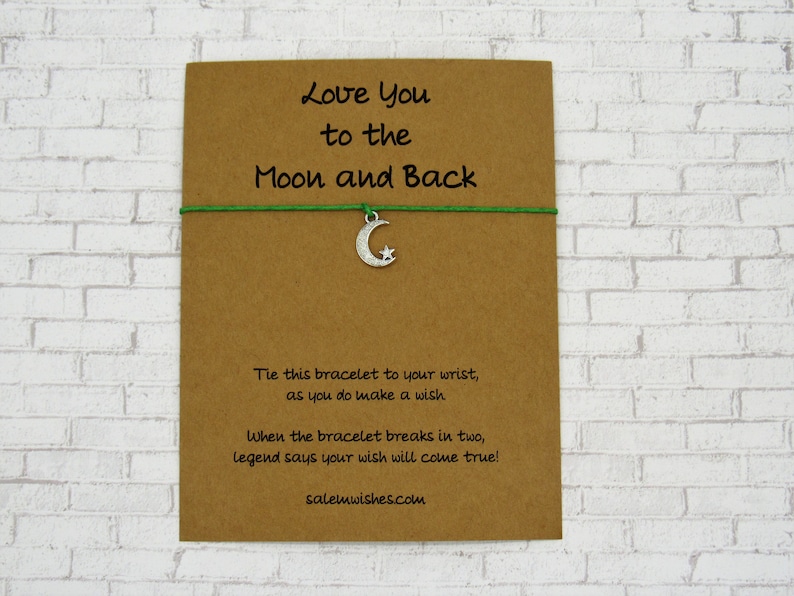 May include: A green string bracelet with a silver crescent moon charm. The card reads "Love You to the Moon and Back". Tie this bracelet to your wrist as you do make a wish. When the bracelet breaks in two, legend says your wish will come true! salemwishes.com