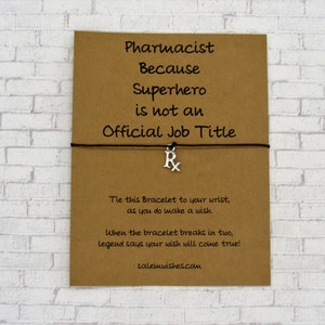 May include: A brown card with the text "Pharmacist Because Superhero is not an Official Job Title" and a black string bracelet with a silver charm that says "Rx". The card also includes instructions for tying the bracelet and making a wish.