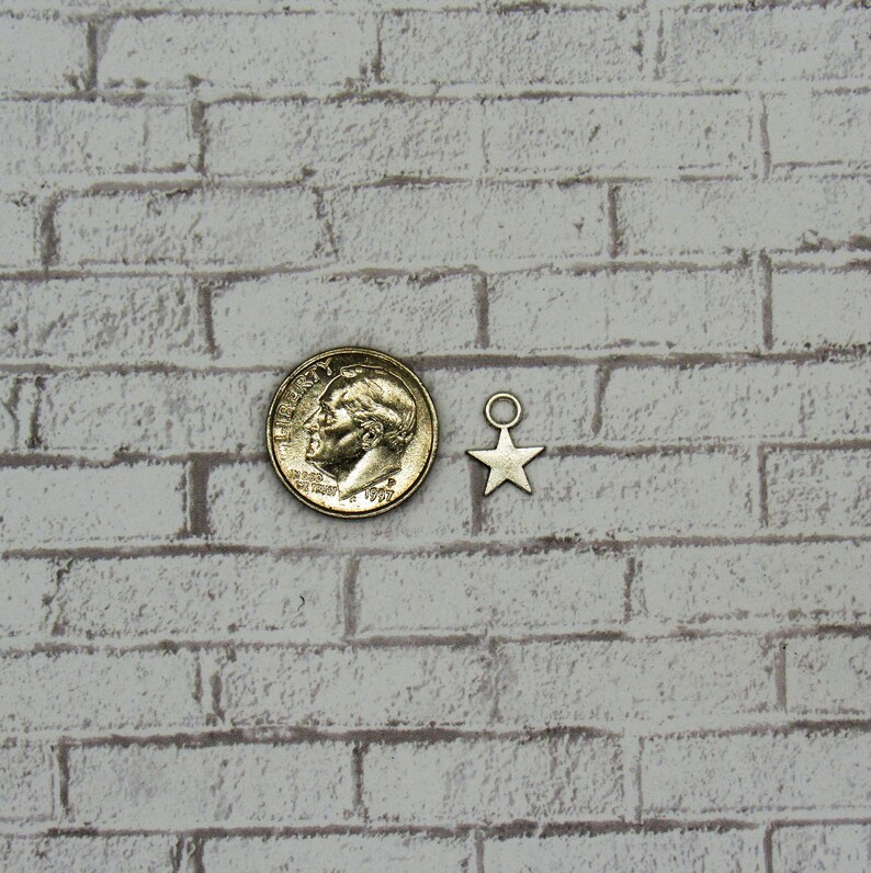 May include: A silver star charm with a jump ring, next to a US dime coin. The star charm is about the size of the dime.