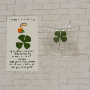 May include: A white card with the text "Happy St. Patricks Day" and a message about a leprechaun escaping a trap. The card is next to a clear plastic bag containing a four-leaf clover.