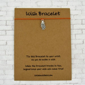 May include: A brown card with the text "Wish Bracelet" printed in black. The card has an orange string attached to it with a silver charm shaped like a jellyfish. The text on the card reads: "Tie this Bracelet to your wrist, as you do make a wish. When the bracelet breaks in two, legend says your wish will come true! salemwishes.com"