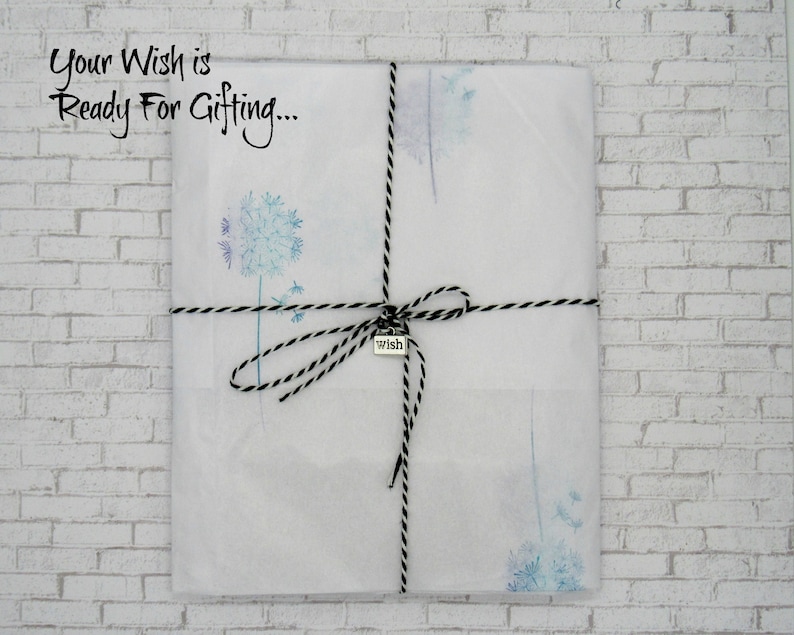May include: A white gift bag with a black and white twine bow. The bag is decorated with a watercolor design of dandelions. The bag has a small silver tag that says "wish". The text "Your Wish is Ready For Gifting..." is written on the bag.