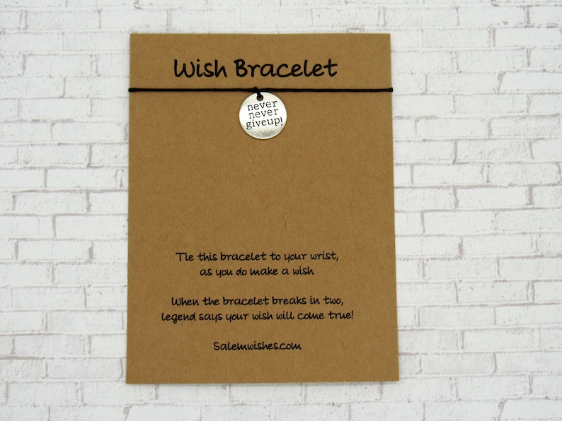 K&ouml;nnte beinhalten: Eine braune Karte mit dem Text "Wish Bracelet" und "never never giveup!" auf einem silbernen Anh&auml;nger. Die Karte enth&auml;lt auch Anweisungen zur Verwendung des Armbands und eine Website-Adresse.