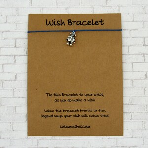 May include: A brown card with the text "Wish Bracelet" printed on it. The card has a blue string tied around it with a silver robot charm hanging from the string. The card also has the text "Tie this Bracelet to your wrist, as you do make a wish. When the bracelet breaks in two, legend says your wish will come true! salemwishes.com" printed on it.