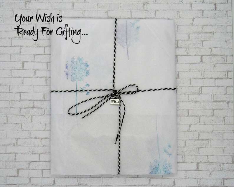May include: A white gift bag with a black and white twine bow and a silver charm that says "wish". The bag is decorated with a watercolor design of dandelion seeds. The text "Your Wish is Ready For Gifting..." is printed on the bag.