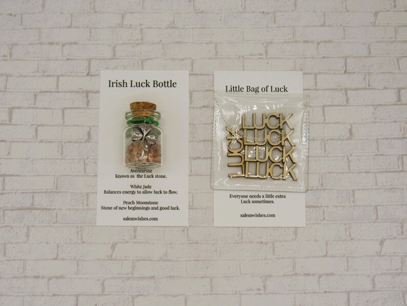 May include: Two cards with a white background and black text. The card on the left shows a small glass bottle with a green shamrock charm inside. The text reads "Irish Luck Bottle" and lists the stones inside the bottle. The card on the right shows a small bag of wooden "LUCK" charms. The text reads "Little Bag of Luck" and says "Everyone needs a little extra luck sometimes".