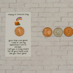 May include: A white card with a green shamrock and rainbow pot of gold illustration. The card reads "Happy St. Patrick's Day". The text on the card reads "Your trap was great. I had to use my leprechaun luck to escape. I left you a lucky charm for all your hard work. See you next year!" There are four Euro coins on a white brick background.