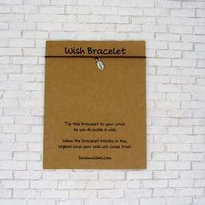 May include: A brown string bracelet with a small silver-toned football charm attached to a rectangular kraft paper card. The card features the text Wish Bracelet and a poem about making a wish, along with the website address Salemwishes.com.