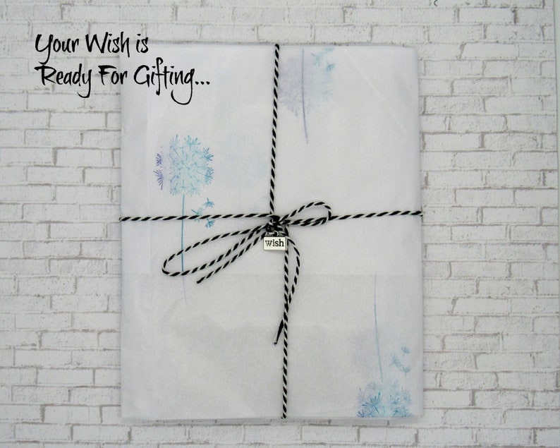 May include: A white gift bag with a black and white twine bow and a silver charm that says "wish". The bag is decorated with a watercolor design of dandelion seeds. The text "Your Wish is Ready For Gifting..." is printed on the bag.