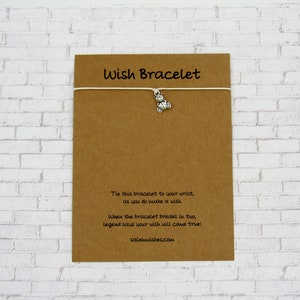May include: A brown card with the text "Wish Bracelet" printed in white. The card has a white string attached to it with a silver charm of a small motorcycle. The text on the card reads: "Tie this bracelet to your wrist, as you do make a wish. When the bracelet breaks in two, legend says your wish will come true! salemwishes.com"