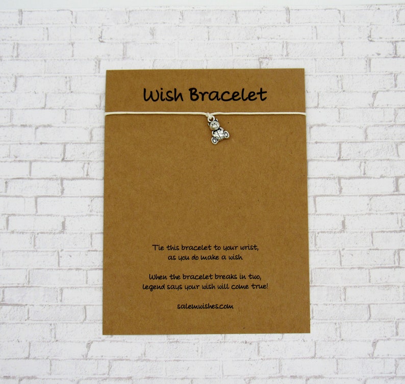 May include: A brown card with the text "Wish Bracelet" printed in white. The card has a white string attached to it with a silver charm of a small motorcycle. The text on the card reads: "Tie this bracelet to your wrist, as you do make a wish. When the bracelet breaks in two, legend says your wish will come true! salemwishes.com"