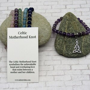 K&ouml;nnte beinhalten: Ein violettes Amethyst-Perlenarmband mit einem silbernen keltischen Knoten-Anh&auml;nger. Das Armband liegt auf einem grauen Stein mit einer wei&szlig;en Karte, auf der "Celtic Motherhood Knot" und "The Celtic Motherhood Knot symbolizes the unbreakable bond and everlasting love that exists between a mother and her children. www.salemwishes.com" steht.