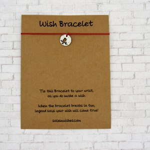 May include: A brown card with the text "Wish Bracelet" printed on it. The card has a red string with a silver charm attached to it. The charm is a bird with a cut-out design. The text on the card reads: "Tie this Bracelet to your wrist, as you do make a wish. When the bracelet breaks in two, legend says your wish will come true! salemwishes.com"