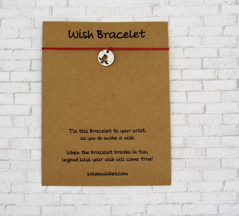 May include: A brown card with the text "Wish Bracelet" printed on it. The card has a red string with a silver charm attached to it. The charm is a bird with a cut-out design. The text on the card reads: "Tie this Bracelet to your wrist, as you do make a wish. When the bracelet breaks in two, legend says your wish will come true! salemwishes.com"