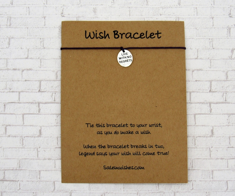 K&ouml;nnte beinhalten: Eine braune Karte mit dem Text "Wish Bracelet" darauf gedruckt. Die Karte hat eine schwarze Schnur mit einem silbernen Anh&auml;nger, auf dem "Live with no regrets" steht. Die Karte enth&auml;lt auch Anweisungen zur Verwendung des Armbands.