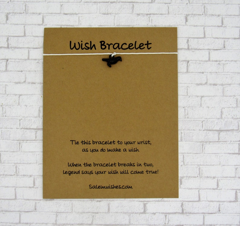 May include: A brown card with the text "Wish Bracelet" printed on it. The card has a white string tied to it with a black bird charm hanging from the string. The text on the card reads: "Tie this bracelet to your wrist, as you do make a wish. When the bracelet breaks in two, legend says your wish will come true! Salemwishes.com"
