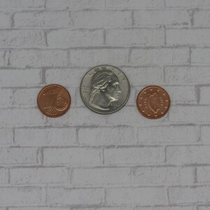 K&ouml;nnte beinhalten: Drei M&uuml;nzen auf einem wei&szlig;en Ziegelhintergrund. Die mittlere M&uuml;nze ist eine silberne US-Viertel-Dollar-M&uuml;nze mit dem Profil von George Washington. Die M&uuml;nzen auf beiden Seiten sind kupferfarben.