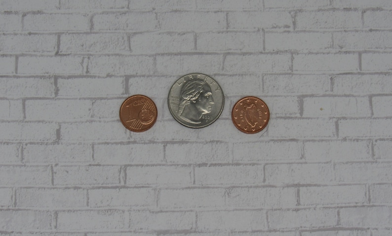 K&ouml;nnte beinhalten: Drei M&uuml;nzen auf einem wei&szlig;en Ziegelhintergrund. Die mittlere M&uuml;nze ist eine silberne US-Viertel-Dollar-M&uuml;nze mit dem Profil von George Washington. Die M&uuml;nzen auf beiden Seiten sind kupferfarben.