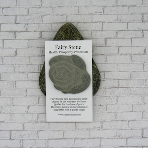 May include: A gray stone with a circular pattern, labeled "Fairy Stone" with the text "Health Prosperity Protection". The stone is on a white card with text about the stone's history and origin.