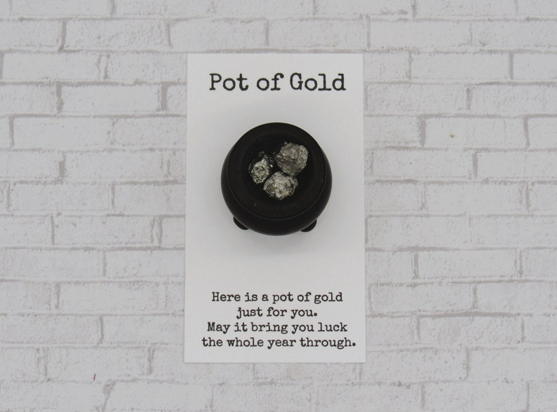 May include: A small black pot with a silver glitter-like substance inside. The pot is on a white card with the text "Pot of Gold" and "Here is a pot of gold just for you. May it bring you luck the whole year through."