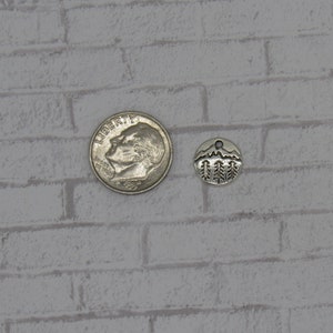 May include: Silver charm featuring a mountain and pine tree design. The charm is approximately the size of a ten pence coin.