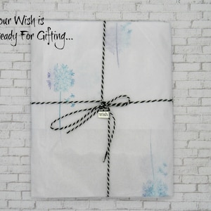 May include: A white gift bag with a black and white twine bow. The bag is decorated with a watercolor dandelion design and has a small silver tag that says "wish". The text "Your Wish is Ready For Gifting..." is written on the bag.