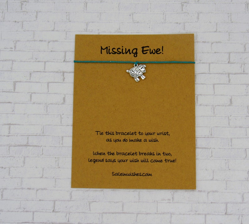 May include: A brown card with the text "Missing Ewe!" and a green string bracelet with a silver sheep charm. The card also includes instructions for making a wish and the website Salemwishes.com.