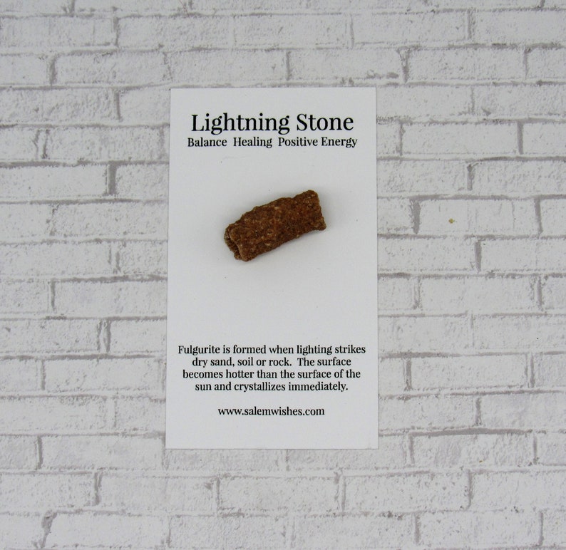 Pode incluir: Uma pedra de raio de fulgurite em um cart&atilde;o branco com texto. A pedra tem uma forma cil&iacute;ndrica &aacute;spera com uma superf&iacute;cie marrom e texturizada. O cart&atilde;o diz "Lightning Stone" e descreve sua forma&ccedil;&atilde;o.