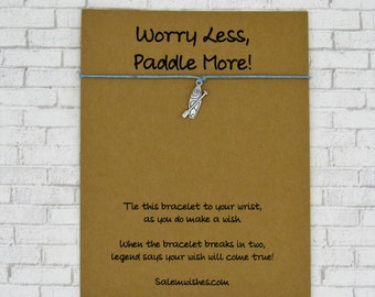 May include: A brown card with the text "Worry Less, Paddle More!" and a silver charm of a paddle board with an oar. The card also includes the text "Tie this bracelet to your wrist, as you do make a wish. When the bracelet breaks in two, legend says your wish will come true! Salemwishes.com".