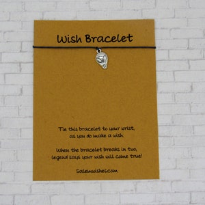 May include: A brown card with the text "Wish Bracelet" printed on it. A black string bracelet with a silver alien charm is attached to the card. The card also includes the text "Tie this bracelet to your wrist, as you do make a wish. When the bracelet breaks in two, legend says your wish will come true! Salemwishes.com"