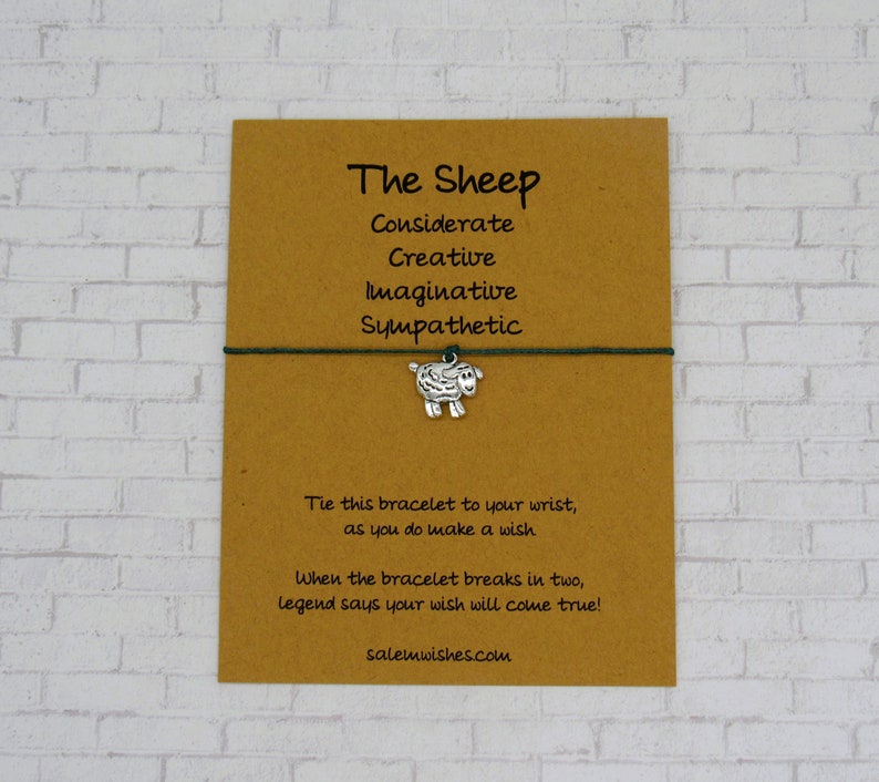 May include: A brown card with the text "The Sheep" and a list of personality traits: considerate, creative, imaginative, sympathetic. A green string bracelet with a silver sheep charm is attached to the card. The text "Tie this bracelet to your wrist, as you do make a wish. When the bracelet breaks in two, legend says your wish will come true! salemwishes.com" is printed on the card.