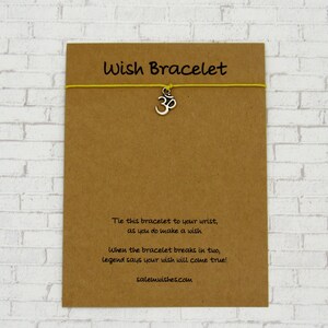 May include: A brown card with the text "Wish Bracelet" and a yellow string bracelet with a silver Om symbol charm. The card also includes the text "Tie this bracelet to your wrist, as you do make a wish. When the bracelet breaks in two, legend says your wish will come true! salemwishes.com".