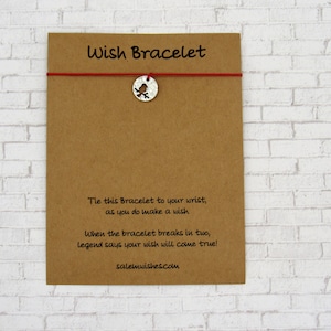 May include: A brown card with the text "Wish Bracelet" printed on it. The card has a red string with a silver charm attached to it. The charm is a bird with a cut-out design. The text on the card reads: "Tie this Bracelet to your wrist, as you do make a wish. When the bracelet breaks in two, legend says your wish will come true! salemwishes.com"