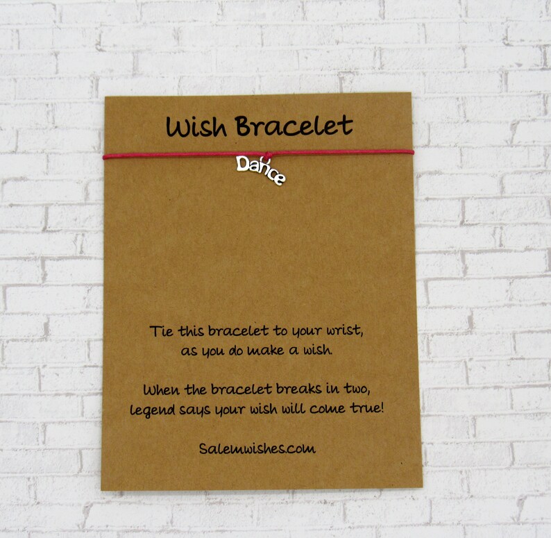 May include: A red string bracelet with a silver charm that says "Dafice". The bracelet is on a brown card with the text "Wish Bracelet" and instructions on how to make a wish.