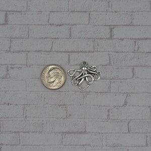 May include: Silver octopus charm pendant, shown next to a US dime for size comparison.