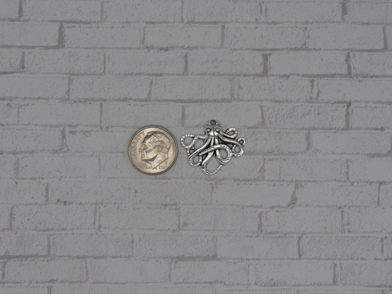 May include: Silver octopus charm pendant, shown next to a US dime for size comparison.