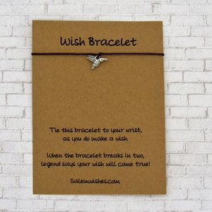 May include: A brown card with the text "Wish Bracelet" printed on it. A brown string bracelet with a silver hummingbird charm is attached to the card. The text on the card reads: "Tie this bracelet to your wrist, as you do make a wish. When the bracelet breaks in two, legend says your wish will come true! Salemwishes.com"