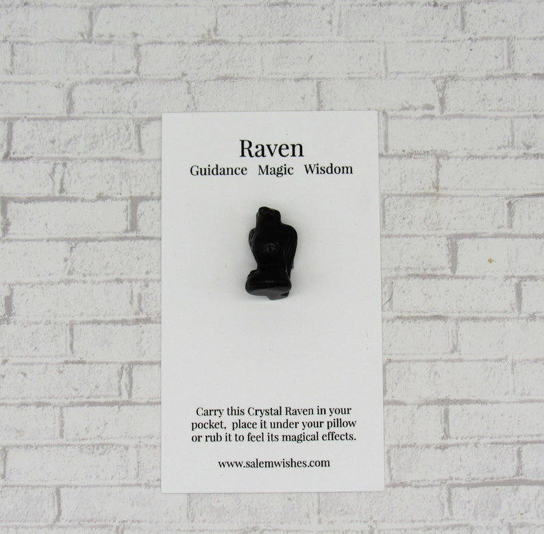Pode incluir: Uma pequena estatueta de corvo preto em um cart&atilde;o branco. O cart&atilde;o diz "Raven Guidance Magic Wisdom". O corvo &eacute; um s&iacute;mbolo de orienta&ccedil;&atilde;o e sabedoria. O cart&atilde;o tamb&eacute;m inclui texto sobre carregar o corvo e um endere&ccedil;o de site.