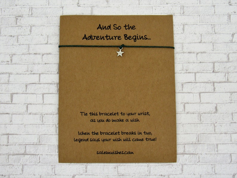 K&ouml;nnte beinhalten: Eine braune Karte mit dem Text "And So the Adventure Begins..." und Anweisungen, das Armband an Ihrem Handgelenk zu binden und einen Wunsch zu machen. Das Armband ist gr&uuml;n mit einem silbernen Sternanh&auml;nger. Die Karte sagt auch "When the bracelet breaks in two, legend says your wish will come true!" und enth&auml;lt die Website salemwishes.com.