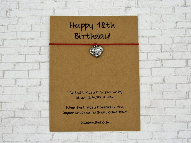 May include: A brown card with the text "Happy 18th Birthday!" and a red string bracelet. The bracelet has a silver heart charm with the number 18. Additional text on the card explains the bracelet's wish-granting legend.