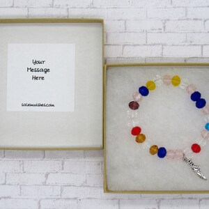 May include: A small gift box with a white card inside that says "Your Message Here" and saleemwishes.com. The box contains a colorful beaded bracelet with a silver charm.