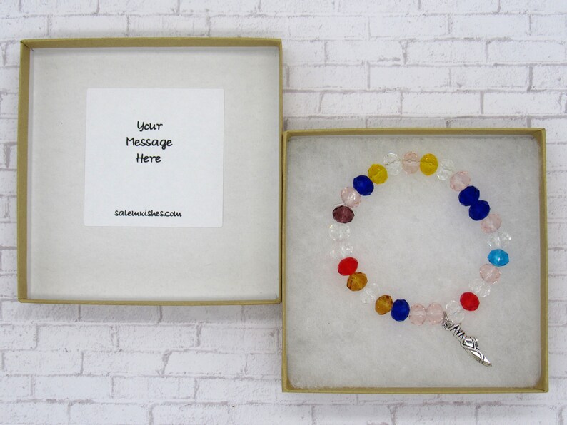 May include: A small gift box with a white card inside that says "Your Message Here" and saleemwishes.com. The box contains a colorful beaded bracelet with a silver charm.