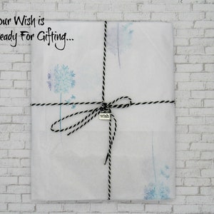 May include: A white gift bag with a black and white twine bow. The bag is decorated with a watercolor dandelion design and has a small silver tag that says "wish". The text "Your Wish is Ready For Gifting..." is written on the bag.