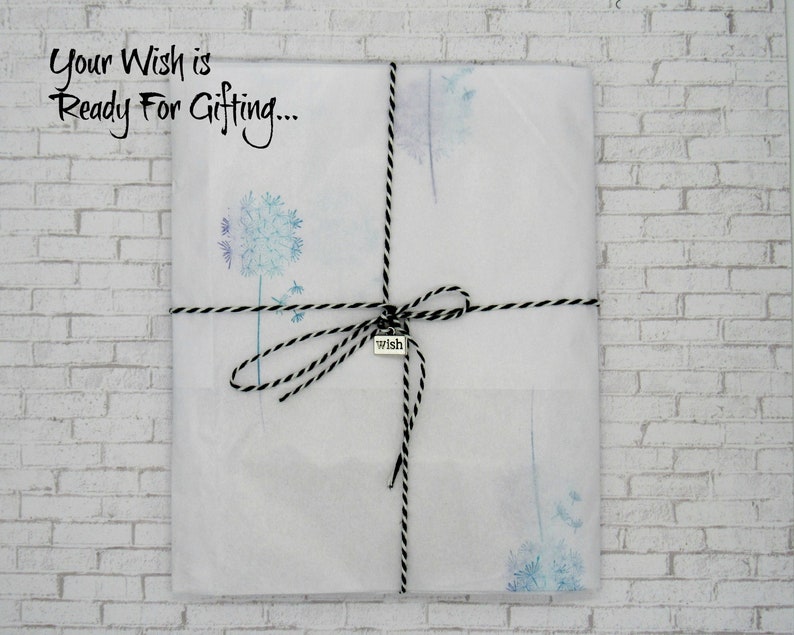 May include: A white gift bag with a black and white twine bow. The bag is decorated with a watercolor dandelion design and has a small silver tag that says "wish". The text "Your Wish is Ready For Gifting..." is written on the bag.