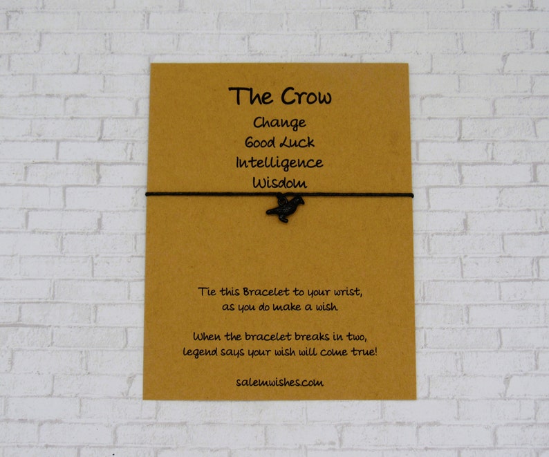May include: A brown card with the text "The Crow" and a list of words: Change, Good Luck, Intelligence, Wisdom. A black crow charm is attached to a black string bracelet. The card also includes instructions for making a wish with the bracelet.