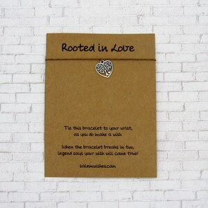 May include: A brown card with the text "Rooted in Love" and instructions for a wish bracelet. The bracelet has a silver charm shaped like a tree inside a heart.