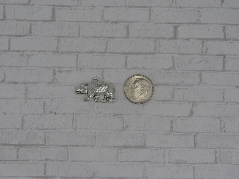 May include: A silver bear charm, shown next to a US dime for size comparison. The bear charm is detailed and has a textured surface.
