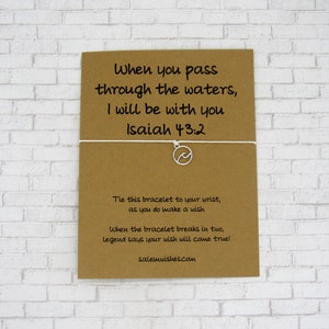 May include: A brown card with white string attached to a silver charm with a wave design. The card has the text "When you pass through the waters, I will be with you Isaiah 43:2" and instructions to tie the bracelet to your wrist and make a wish. The card also says "When the bracelet breaks in two, legend says your wish will come true!" and includes the website salemwishes.com.