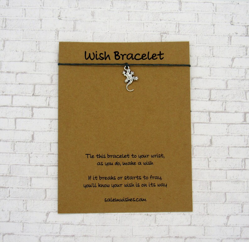 May include: A brown card with the text "Wish Bracelet" printed in black. The card has instructions on how to use the bracelet, which includes a silver lizard charm. The text on the card reads: "Tie this bracelet to your wrist, as you do, make a wish. If it breaks or starts to fray, you'll know your wish is on its way. salemwishes.com"